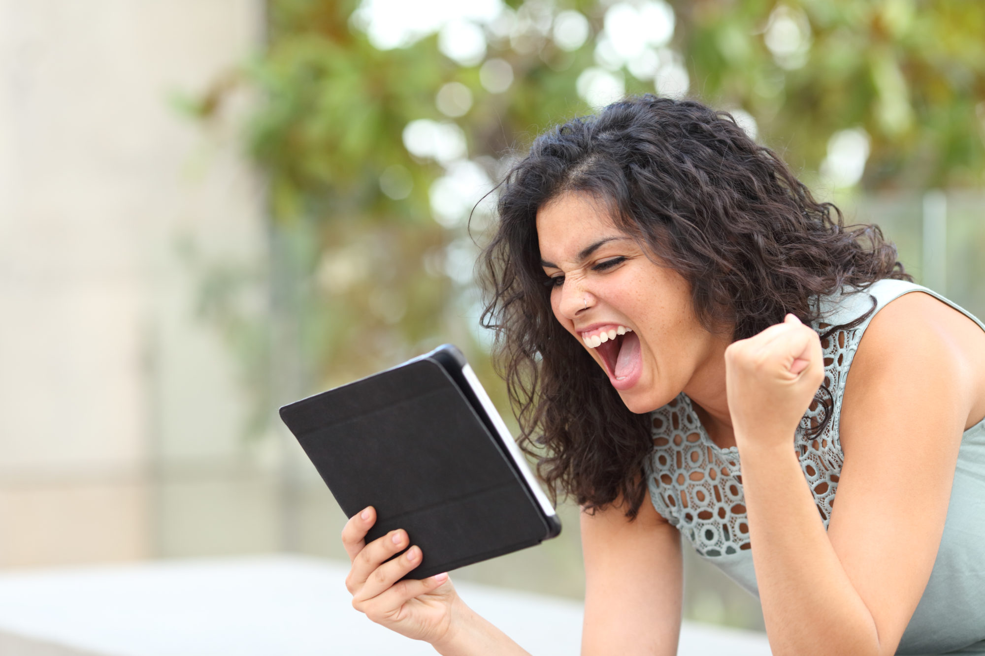Excited girl holding a tablet and making a fist in celebration